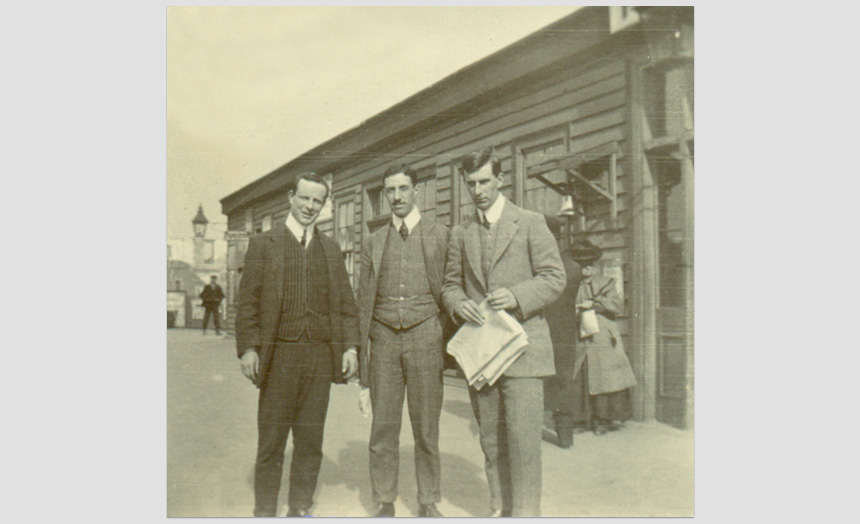 Edward Theomin with 2 other young men outside a (Dunedin) Railway station. One of a set of ten snapshots of a picnic outing, (early 1900's).